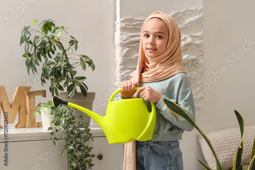 Photography Little Muslim girl in hijab watering houseplant at home