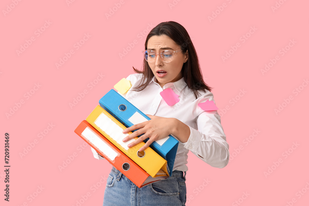 Stressed young businesswoman with sticky notes and document folders on pink background Stressed young businesswoman with sticky notes and document folders on pink background