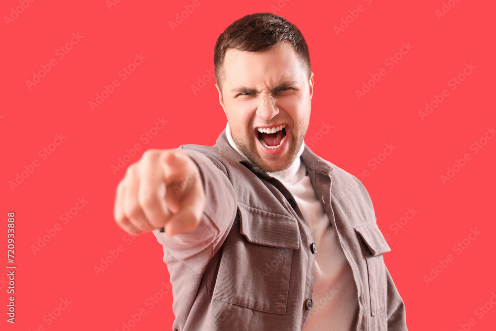 Angry young man pointing at viewer on red background, closeup. Accusation concept Angry young man pointing at viewer on red background, closeup. Accusation concept