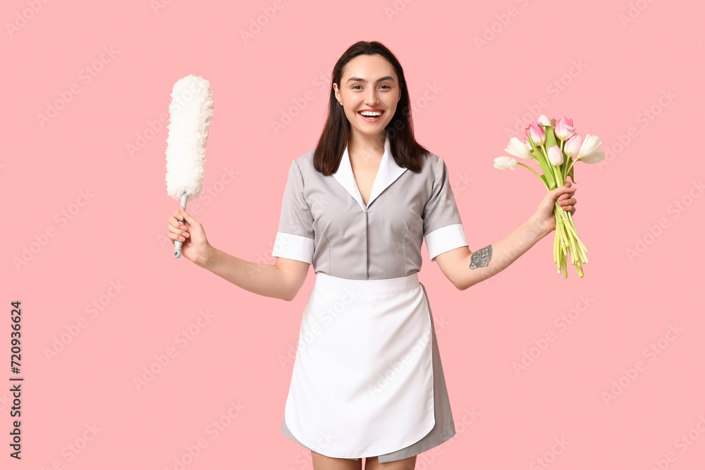 Portrait of young female janitor with bouquet of flowers and pp-duster on pink background. International Women's Day Portrait of young female janitor with bouquet of flowers and pp-duster on pink background. International Women's Day