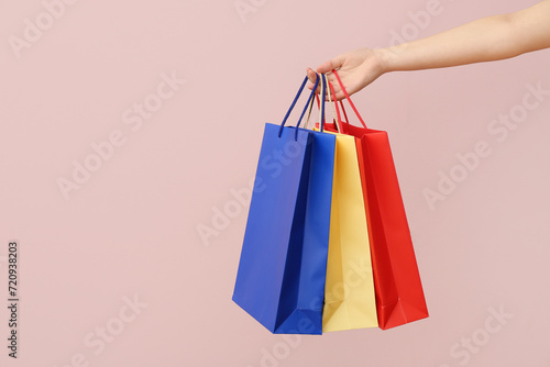 Female hand with paper shopping bags on light background. Valentine's Day celebration