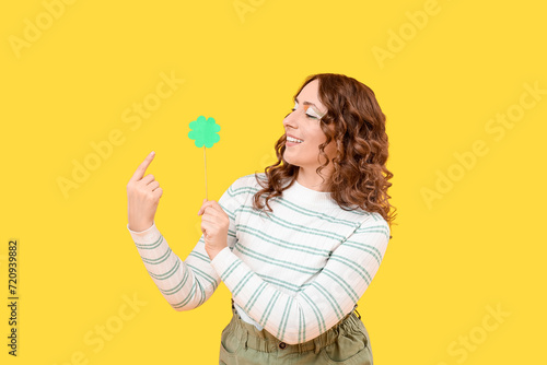 Happy woman with paper clover on yellow background. St. Patrick's Day