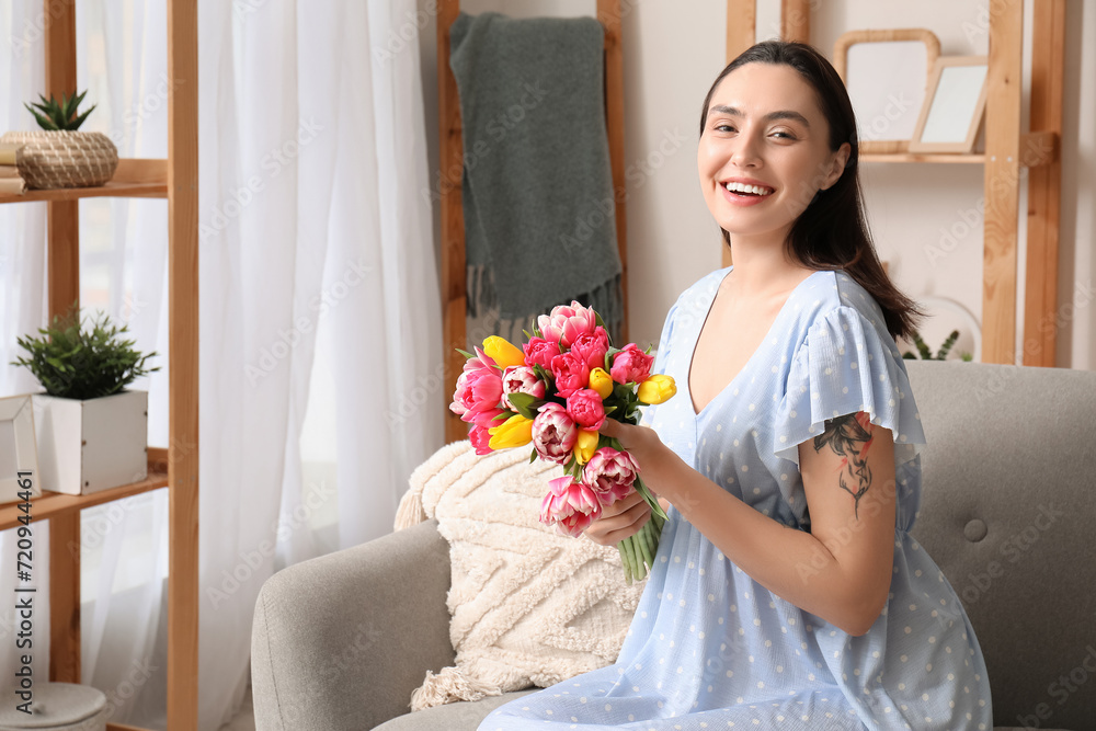 Happy young woman with bouquet of beautiful tulips on sofa at home. International Women's Day