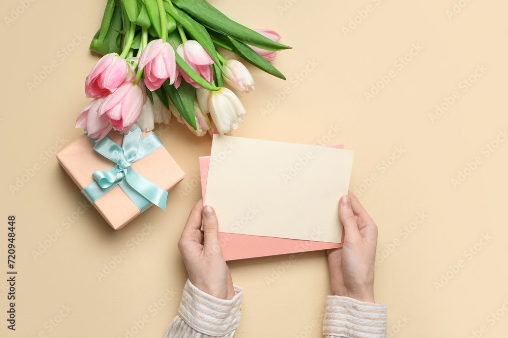 Female hands with blank card, gift box and bouquet of beautiful tulips on yellow background. International Women's Day Female hands with blank card, gift box and bouquet of beautiful tulips on yellow background. International Women's Day