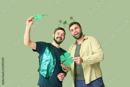 Young men in headband with green beards holding clover on green background. St. Patrick's Day celebration photo