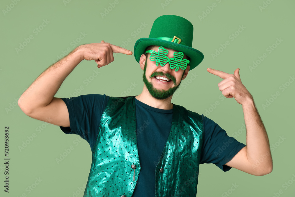 Young man in leprechaun hat with green beard pointing at decorative glasses in shape of clover on green background. St. Patrick's Day celebration Young man in leprechaun hat with green beard pointing at decorative glasses in shape of clover on green background. St. Patrick's Day celebration