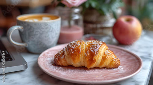 Cozy breakfast scene with fresh croissant on a pink plate  cup of coffee  laptop  and a smoothie on a wooden table.