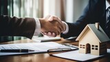 Close-up of a professional handshake over a house model, symbolizing a real estate agreement.
