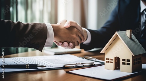 Close-up of a professional handshake over a house model, symbolizing a real estate agreement. photo