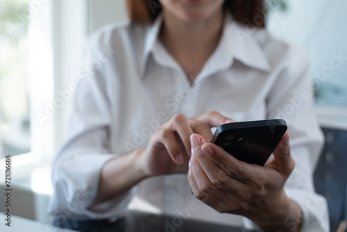 Close up of businesswoman using mobile smart phone during working on laptop computer at office. Asian business woman hand holding smartphone, connecting the internet