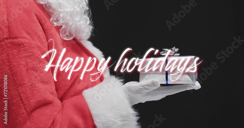 Happy holidays text over father christmas holding present on black background