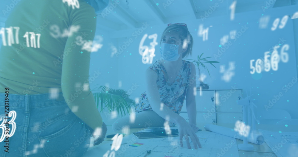 Obraz premium Image of floating numbers with colleagues in office wearing face masks