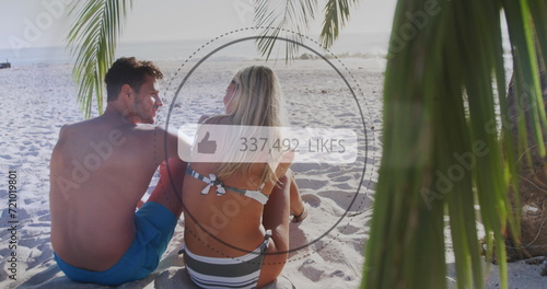 Like icons with increasing numbers against rear view of caucasian couple sitting on the beach