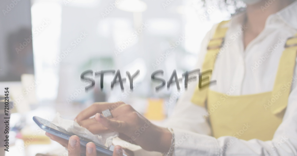 Image of flashing words with woman disinfecting smartphone in office wearing face masks