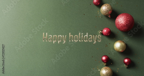 Happy holidays text with glittery christmas baubles on green background