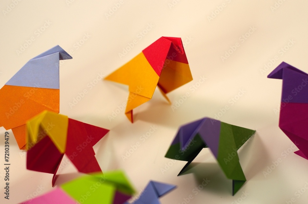 Overhead view of several origami birds in the middle of attacking a blue origami bird. In the background an orange and red bird stands apart, and several of the attack birds are turned as if noticing. Overhead view of several origami birds in the middle of attacking a blue origami bird. In the background an orange and red bird stands apart, and several of the attack birds are turned as if noticing.