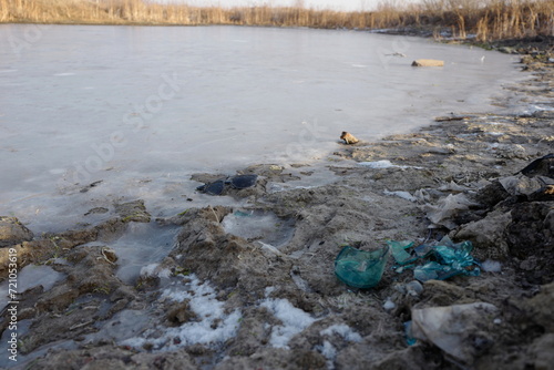 Environmental pollution with garbage. A broken bottle, abandoned sunglasses and trash on the shore of a pond.