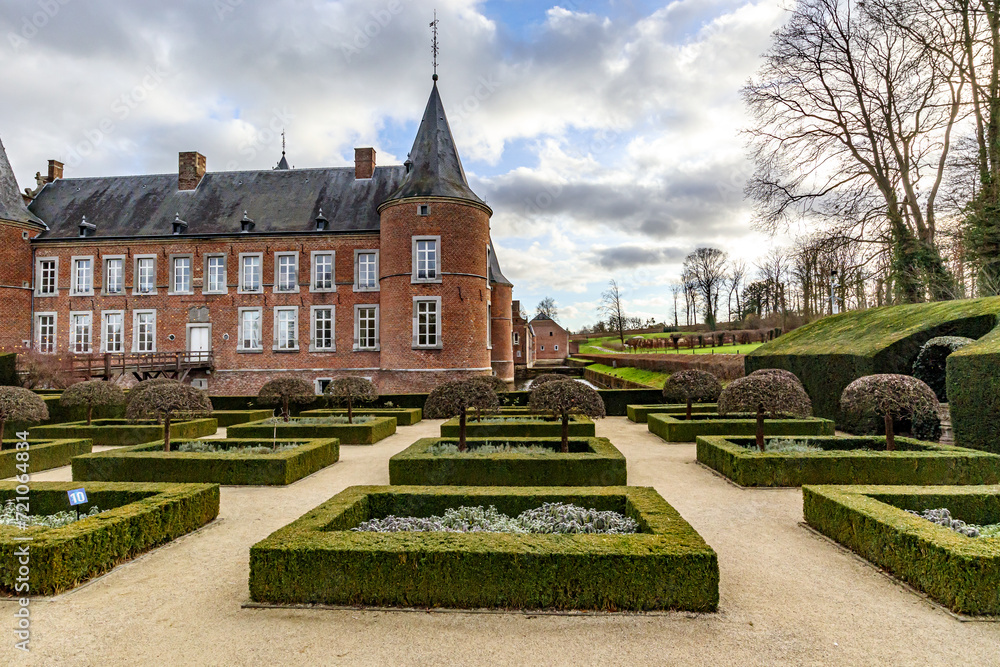 French garden with bushes and small trees, 16th century Alden Biesen Castle in background, bare trees, windows, brick walls, gable roof and circular towers, cloudy day in Bilzen, Limburg, Belgium French garden with bushes and small trees, 16th century Alden Biesen Castle in background, bare trees, windows, brick walls, gable roof and circular towers, cloudy day in Bilzen, Limburg, Belgium