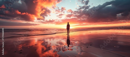 Solitary young man on beach with stunning sunset backdrop.