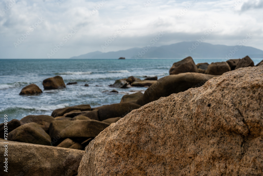 Coastal waves crash against monumental granite boulders lining shore. majestic seascape features vast expanse of rocks, under turbulent, cloud-laden sky, untamed natural panorama