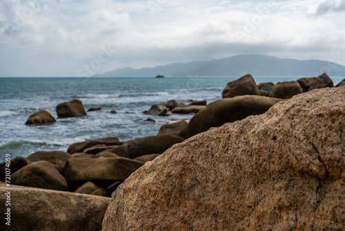 Coastal waves crash against monumental granite boulders lining shore. majestic seascape features vast expanse of rocks, under turbulent, cloud-laden sky, untamed natural panorama