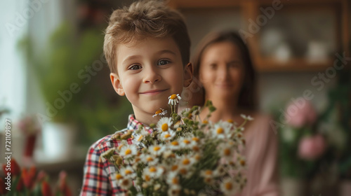 A 10-year-old boy in a checkered shirt stands with a bouquet of flowers for h...