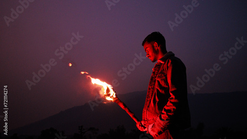 Image of brave man holding burning stick while moving in darkness. Young man holding a fire stick on the mountain top near the sea. 
