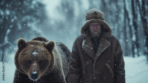 A stern Russian man in a ushanka hat walks with a bear in a Siberian winter forest photo