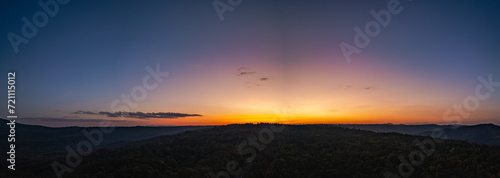 Aerial panorama view  A breathtaking sunset paints the sky with vibrant hues of orange and red  .casting a warm glow over the majestic mountains in a tranquil evening landscape.