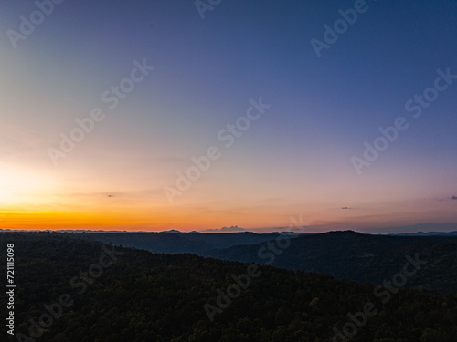 Aerial view A breathtaking sunset paints the sky with vibrant hues of orange and red, .casting a warm glow over the majestic mountains in a tranquil evening landscape.