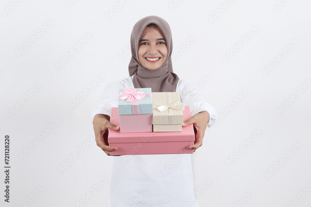 A beautiful Asian Muslim woman is holding out several gifts of various colors while smiling showing her teeth A beautiful Asian Muslim woman is holding out several gifts of various colors while smiling showing her teeth