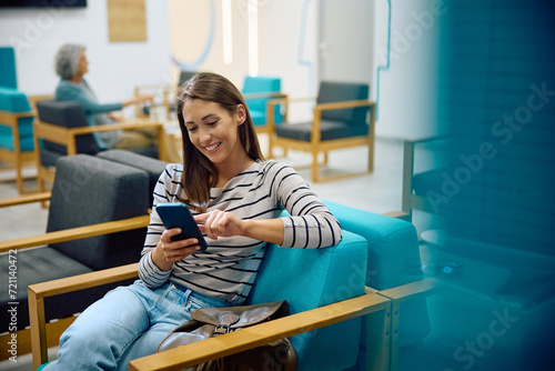 Young happy woman using cell phone in waiting room at doctor's office.