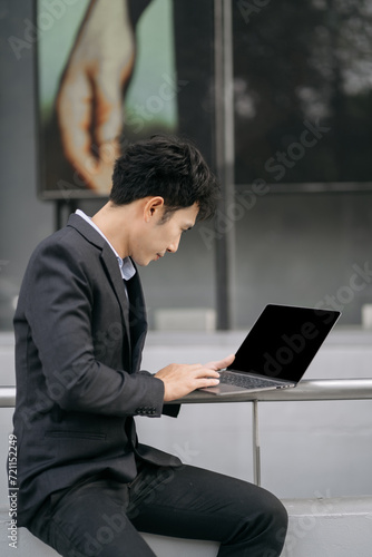 Asian male businessman use smartphone and holding laptop computer, Walk enjoy smiling while doing commuting at business center.