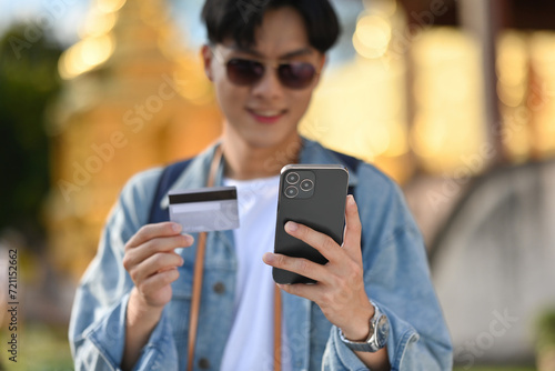 Close-up of a Young Asian tourist smiling, Happy paying by credit card on his mobile phone, Concept of travel and transportation insurance