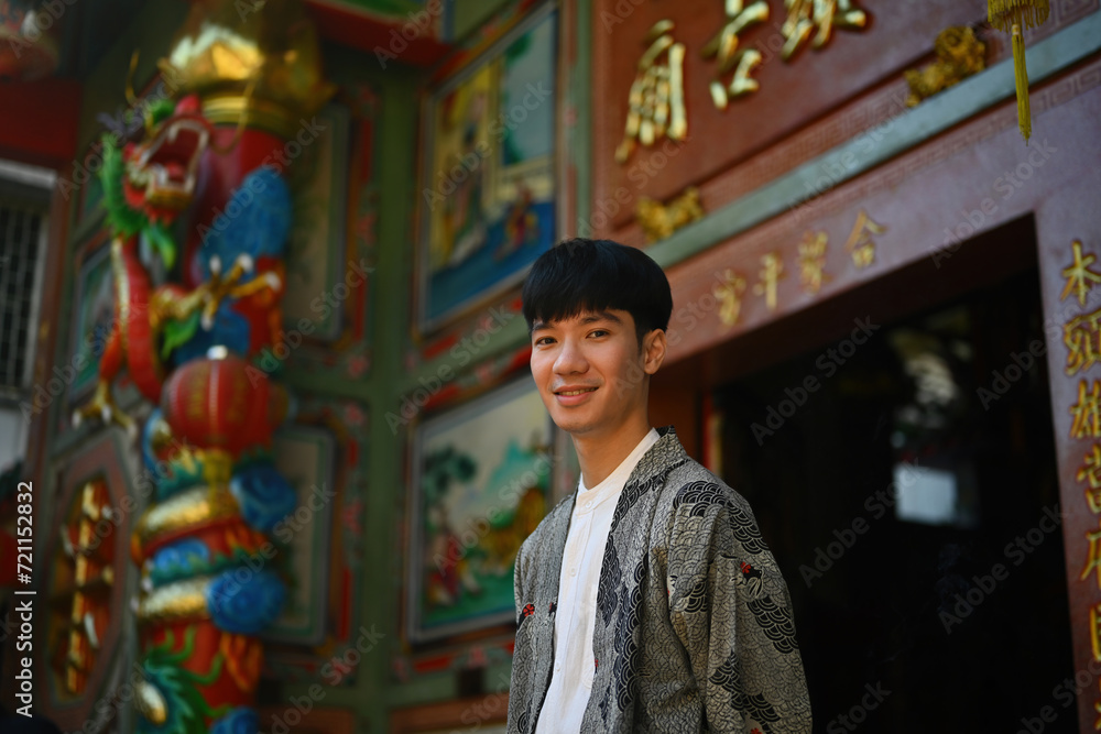 Portrait of a happy and smiling young Asian man wearing a robe standing in front of the entrance to a Chinese shrine