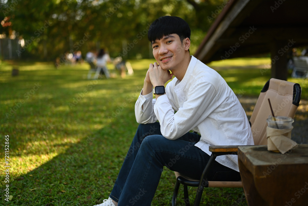 Portrait of Smiling Young Asian man sitting and relaxing on the camping chair, Outdoor recreation concept Portrait of Smiling Young Asian man sitting and relaxing on the camping chair, Outdoor recreation concept