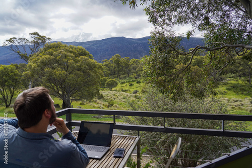 A man working remotely from his balcony looking over bushland and mountains
