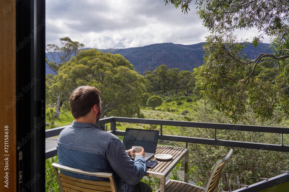 A man working remotely from his balcony looking over bushland and mountains A man working remotely from his balcony looking over bushland and mountains