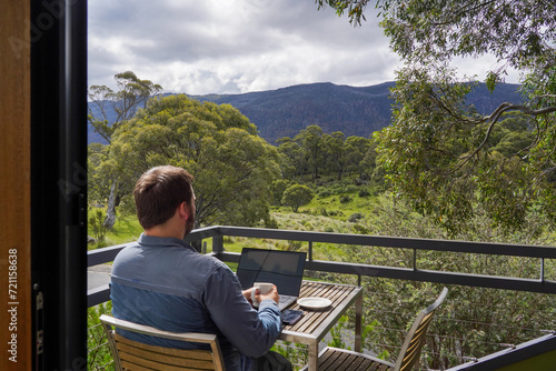 фотографія A man working remotely from his balcony looking over bushland and mountains