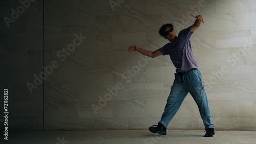 Skilled smart street dancer practice b-boy movement in building with gray background. Young handsome attractive choreographer perform energetic and active movement. Outdoor sport 2024. Sprightly.