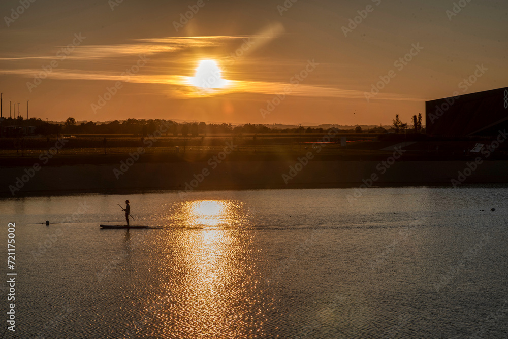 Silhouette of men on sup board with oar in hands on lake in evening with magnificent sunset in background Silhouette of men on sup board with oar in hands on lake in evening with magnificent sunset in background