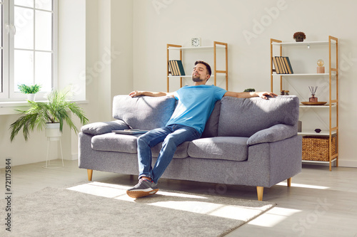 Foto Young relaxed man sitting on comfortable couch in the living room at modern home and having a rest from a work with closed eyes