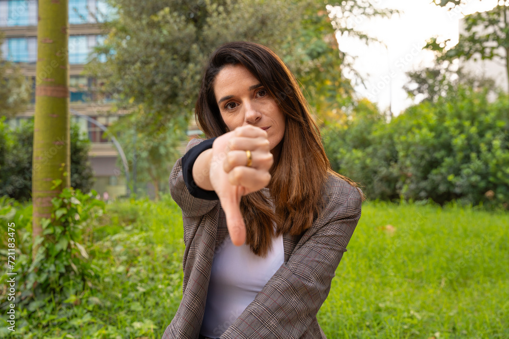 Close-up of a happy young Caucasian woman pointing with her thumbs down. Angry facial expression. Close-up of a happy young Caucasian woman pointing with her thumbs down. Angry facial expression.