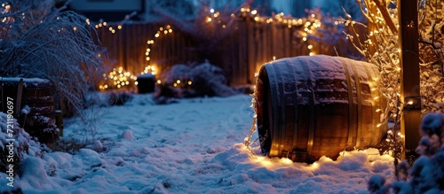 Nighttime yard featuring snow-covered  fairy light-adorned wooden barrel.