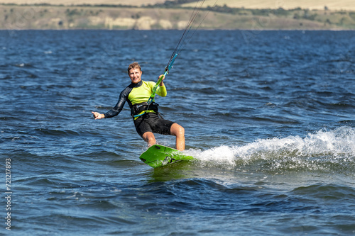 Young adult caucasian fit male person enjoy riding kite surf board in sun uv protection suit on bright sunny day against blue sky at sea or ocean shore. Watersport adrenaline fun adventure acitivity © Kirill Gorlov