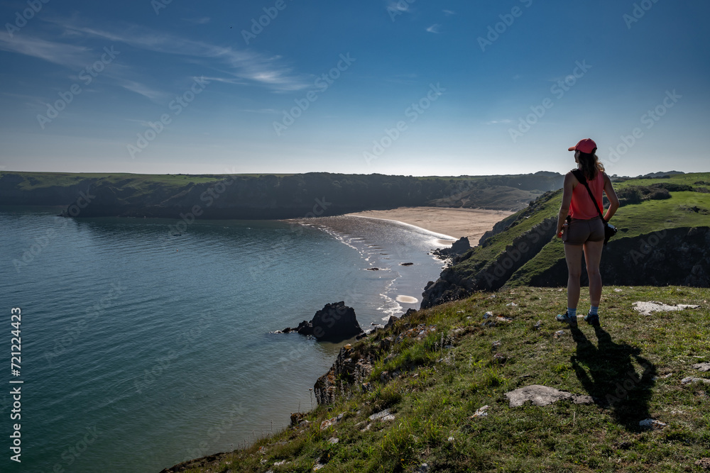 Young Woman Looks Over Atlantic Coast And Barafundle Bay Beach In Wales, Pembrokeshire, United Kingdom