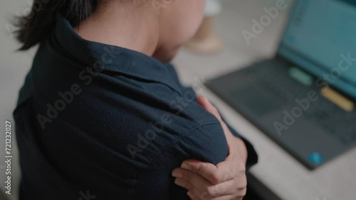 Close-up of tired woman having shoulder pain while working on laptop while sitting at table in modern office.