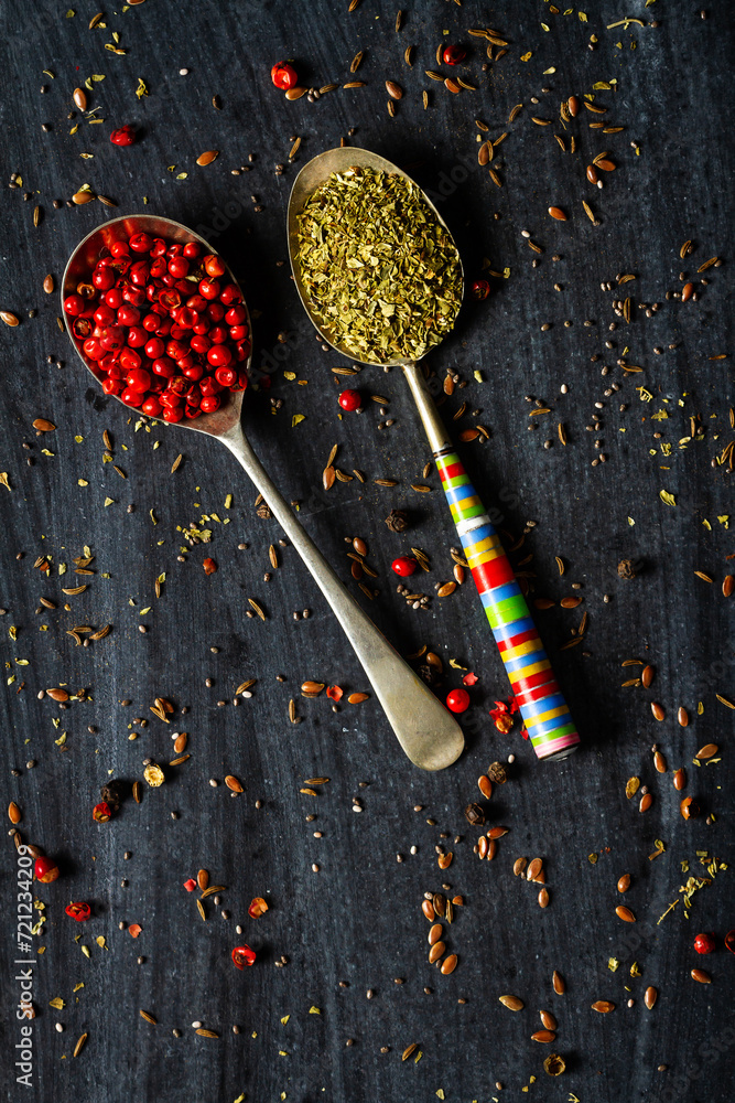 Old metal spoons with oregano and red peppercorn on black background Old metal spoons with oregano and red peppercorn on black background