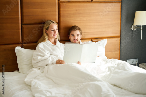 Waking up guy and girlfriend study the menu in bed