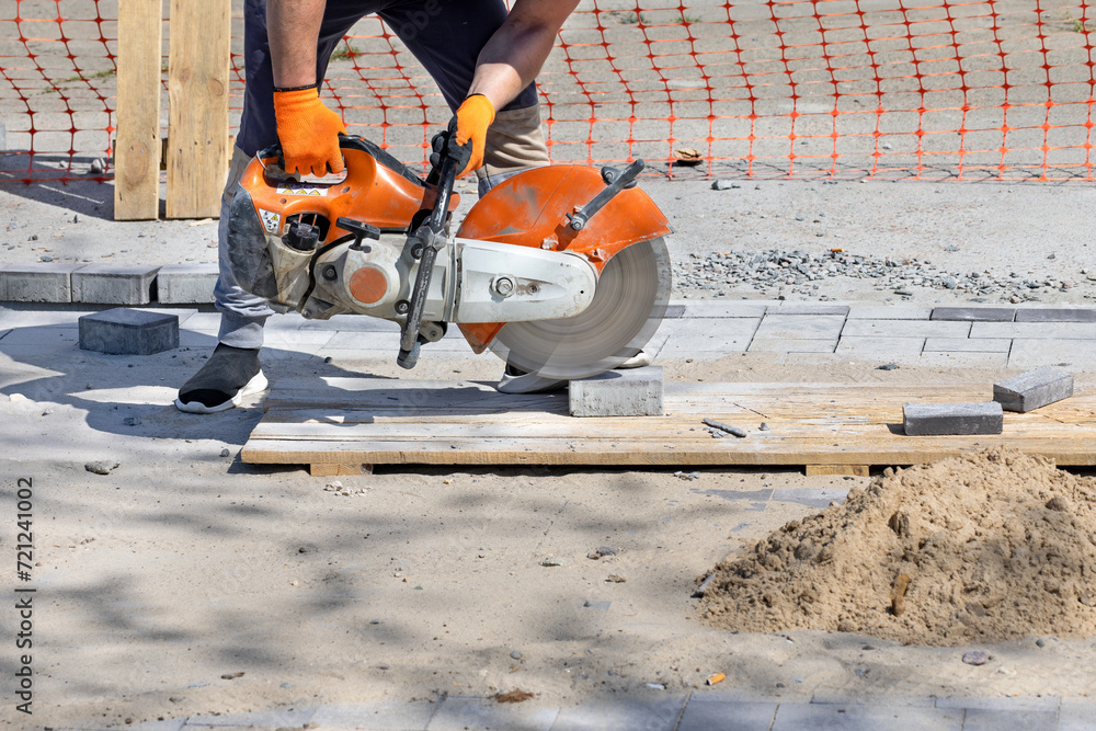 A worker cuts paving blocks at the workplace using a cutting saw and a diamond blade.